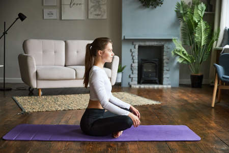 Young girl does yoga and sports at home on the mat