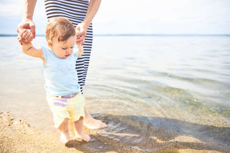 Mom learns to walk little baby on the sand at the beachの写真素材