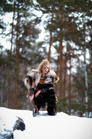 Beautiful blonde Viking dressed in leather armor with melee weapon in snow forest