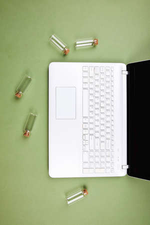 Open white laptop on an isolated green background with empty glass flasks. Top view.