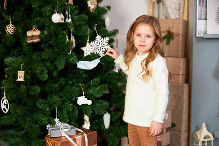 A little cute girl in white eco dress up Christmas tree with a medical maskの写真素材