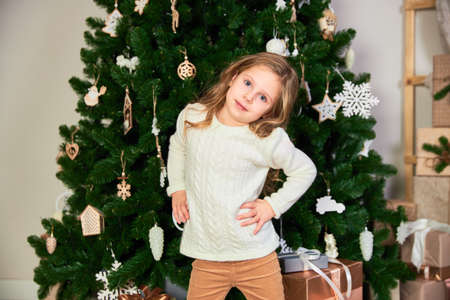 A girl in white eco dress dressed up as a Christmas girl. Theres a green Christmas tree and presents in the back.の写真素材