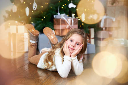 The girl is sitting in the room, behind a beautiful Christmas tree with gifts. Around the garland.の写真素材