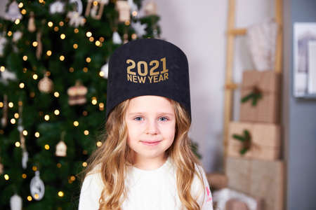 The girl put on a black gift with a gold inscription 2021, behind the Christmas tree with giftsの写真素材