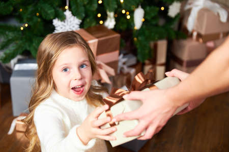 Girl receives gift from mom for Christmas, girl happy and looks into cameraの写真素材