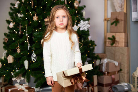 The girl received a christmas present. The girl is upset and looks into the camera. Theres a green Christmas tree in the room with gifts.の写真素材