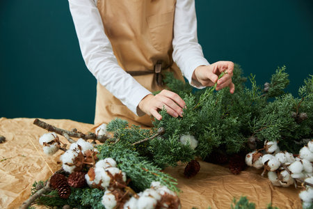 A female florist makes a wreath or bouquet of branches of spruce, cones and flowersの写真素材
