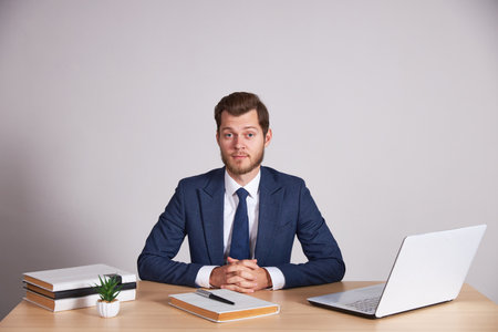 A businessman in a blue business suit sits at his desk, looks into the camera and crosses his arms.の写真素材