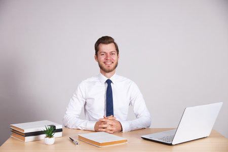A businessman in a white shirt and blue tie sits at his desk and looks into the camera.の写真素材