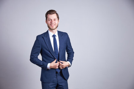 A man in a blue office suit stands against a white background and smiles.の写真素材