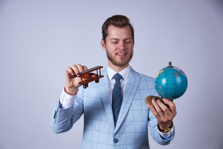 A man in a blue suit on a white background is holding a toy plane and a globe. The plane is flying to the globe.の写真素材