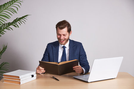 A businessman in a blue business suit holds a book and smiles. White background. Looks into the book.の写真素材