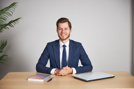 The businessman sits at his desk on a white blank background, crosses his arms and looks into the camera, smiling.の写真素材