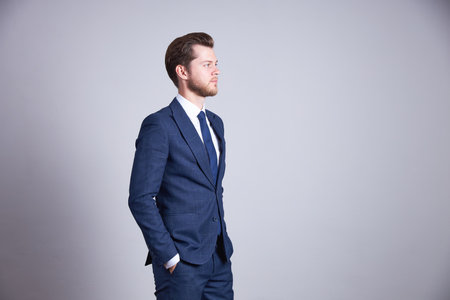 A businessman in a blue business office suit holds his hands in his pockets and looks to the side with a serious face.の写真素材