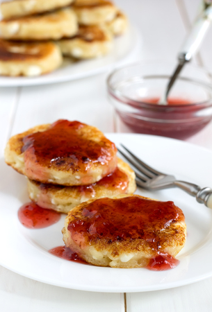 Traditional russian cottage cheese pancakes with sweet berry sauce on a white table. Homemade fritters of curd for breakfast.の写真素材