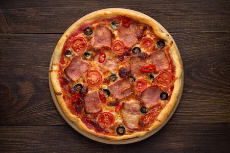 Homemade italian pizza with ham, tomatoes, olives, cheese on dark rustic wooden background. Traditional dish of mediterranean cuisine. Top view.の写真素材