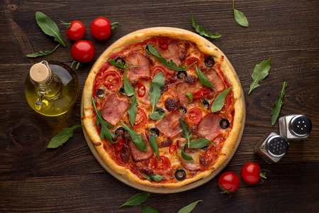 Traditional italian pizza with ham, cheese, tomatoes and olives on rustic wooden background. Top view.の写真素材