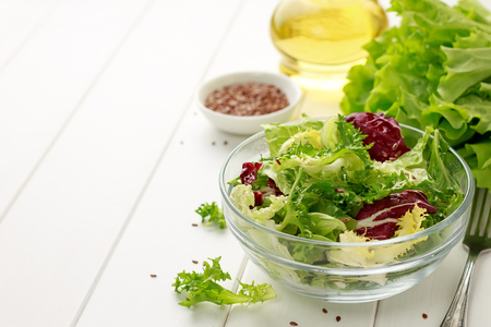 Bowl of fresh mixed salad with flax seeds and oil on white wooden background. Concept of healthy food. Copy space.の写真素材