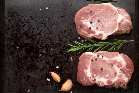 Two raw pork steak on dark rustic metal oven-tray with rosemary and spices. Top view, copy space.の写真素材