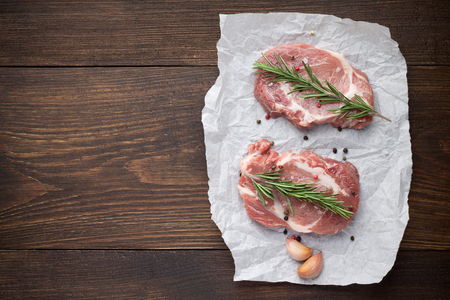 Two raw pork steak on parchment with spices on vintage wooden background. Top view, copy space.の写真素材