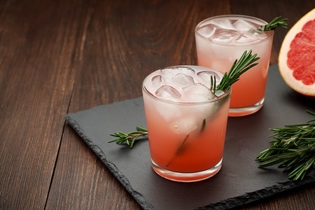 Two glasses of citrus summer drink with grapefruit and rosemary on dark background. Detox fruit cocktail with ice. Copy space.の写真素材