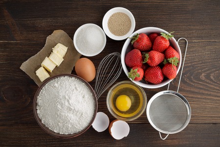Ingredients for recipe of strawberry cake or pie on dark wooden background. Products ready to cooking homemade berry pastry. Top view.の写真素材