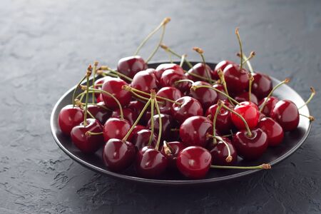 Fresh sweet cherry in black plate on dark stone table. Summer juicy vitamin dessert for healthy diet.の写真素材