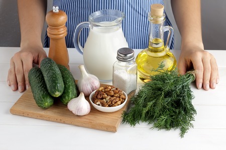 Fresh ingredients for cooking tarator with female hands on white wooden table in the kitchen. Step by step recipe for bulgarian summer cold soup.の写真素材