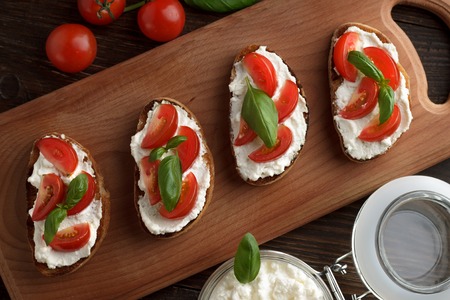 Homemade bruschetta with cheese, tomato and basil on cutting board. Flat lay, closeup.の写真素材