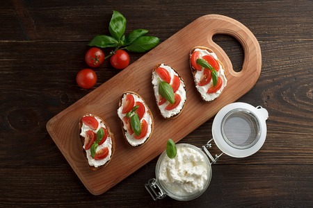 Bruschettas with cheese, tomato and basil on cutting board on wooden rustic background. Top view.の写真素材