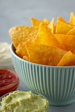 Nachos or tortilla in blue bowl with dipping sauces on gray table. Concept of unhealthy fast food, closeup.の写真素材