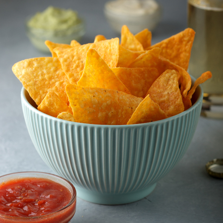 Concept of unhealthy snack food. Spicy nachos in blue bowl on the gray table with dipping.の写真素材