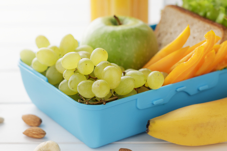 Lunch box with healthy snacks on white wooden background. Plastic container with sandwich, fruits and nuts closeup.の写真素材