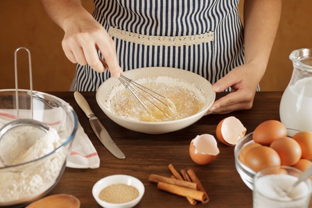 Woman mixes flour with eggs and milk in ceramic bowl on the kitchen. Step by step pastry recipe.の写真素材