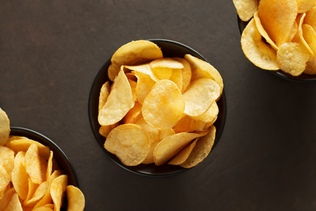 Potato chips in black bowls on brown background. Unhealthy vegan fast food. Top view with copy space.の写真素材
