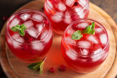Cranberry refreshment cocktail with mint leaves and ice cubes on the wooden cutting board. Three glasses with cold summer berry drink.の写真素材