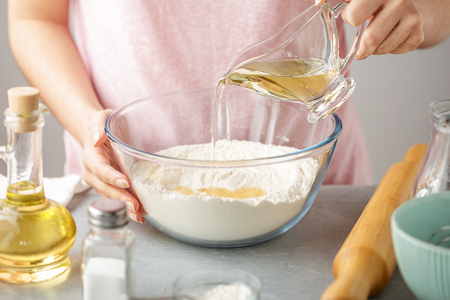 Female hands pour oil into bowl with flour, baking powder and salt. Step by step recipe of homemade mexican tortillas.の写真素材