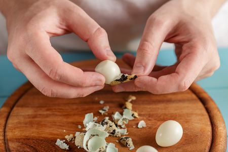 Hands peel boiled quail eggs from shell under wooden cutting board, close-up.の写真素材