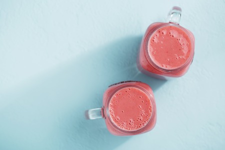 Two mason jars with strawberry smoothie on blue pastel background.の写真素材