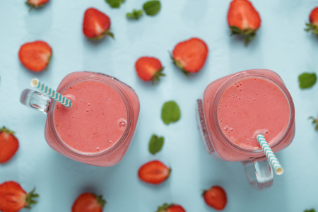 Mason jars with strawberry smoothie of milkshake on blue table with berries halfs.の写真素材