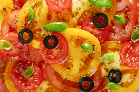 Vegetable background or texture of red and yellow tomato slices, olives and basil top view.の写真素材