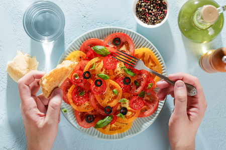 Male hands hold fork and piece of bread for and ready to eat tomato salad top view.の写真素材