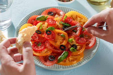 Male hands eat tomato salad with piece of bread with a fork. Personal point of view, pov.の写真素材