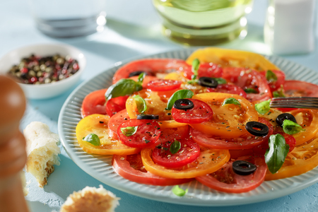 Vegetarian tomato carpaccio with olives and basil on blue plate ready to eat. Concept of healthy food.の写真素材