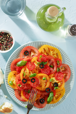 Fresh salad of red and yellow tomato slices on the plate on pastel blue background top view.の写真素材