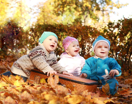 Three cheerful childre in nature sitting in open suitcase. Outings - the forest in autumn. Nearby are big hare toyの写真素材