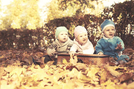 Three cheerful childre in nature sitting in open suitcase. Outings - the forest in autumn. Nearby are big hare toyのeditorial素材