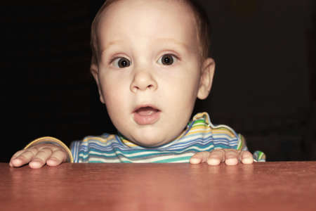 surprised little boy peeking from the tableの写真素材