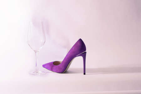 purple high-heeled shoes and a glass of wine. A glass of and womens shoes with heels.の写真素材
