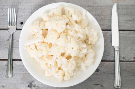 Vegetarian concept with a big plate of raw cauliflower and a knife and fork against vintage wooden backgroundの写真素材
